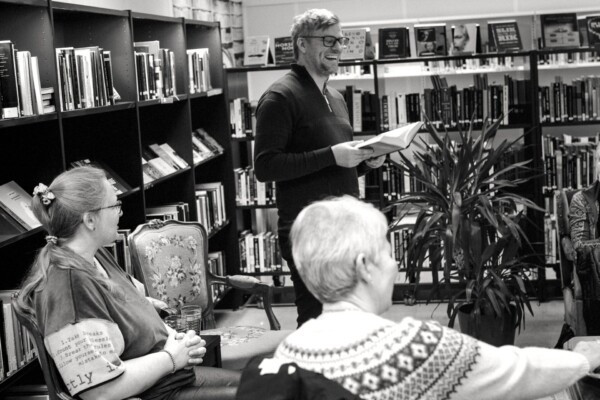 Foto: Mann leser høyt fra bok foran et publikum