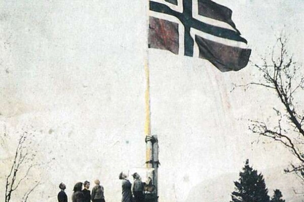 Gammelt foto av folk som ser opp på det norske flagget på en flaggstang.